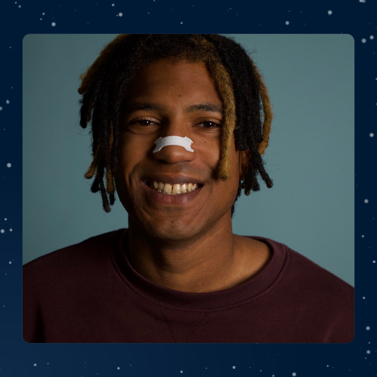 Real photo: a smiling man wearing the white Resty Minty nasal strip on the bridge of his nose, on a navy background with drawn snow.