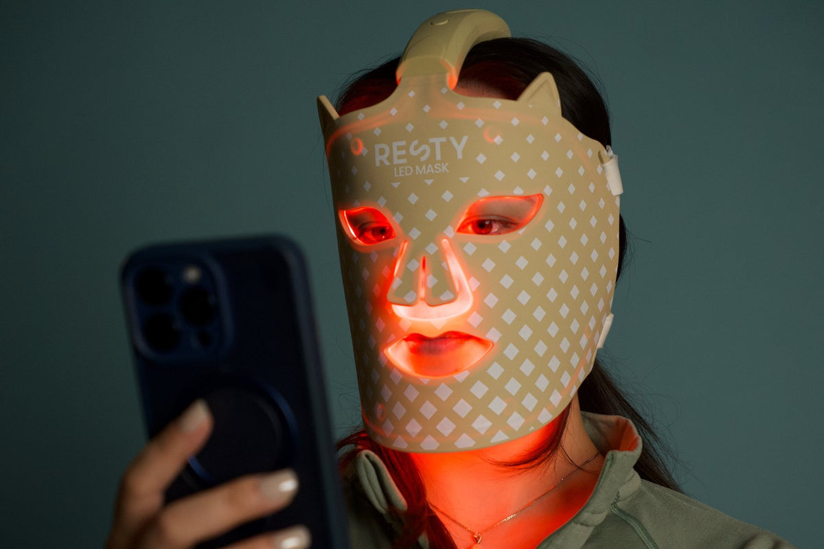 Kvinne med en lysende Resty LED-ansiktsmaske som holder en telefon