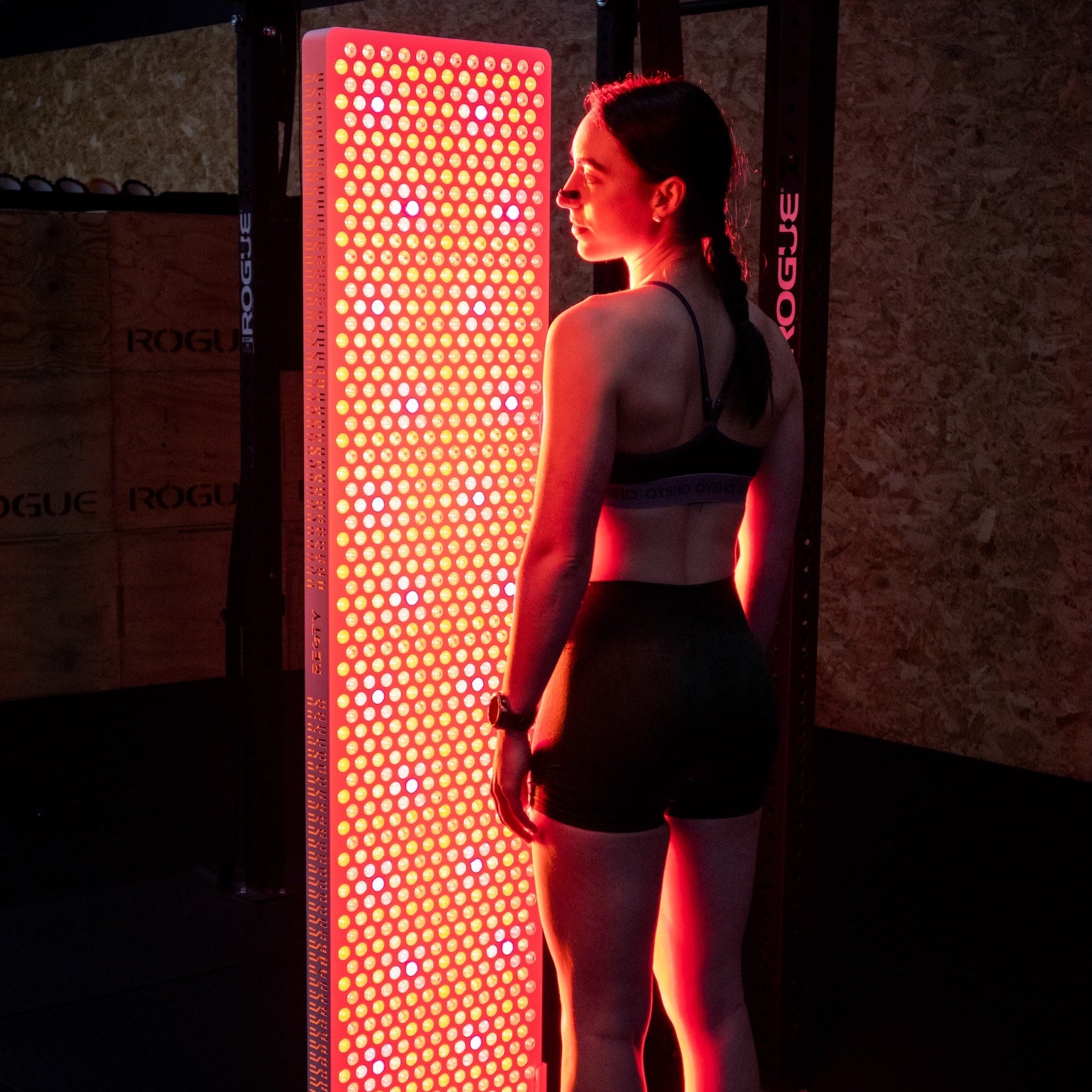 Mulher em pé junto a um painel de luz vermelha Resty MARS 2000 iluminado num ginásio