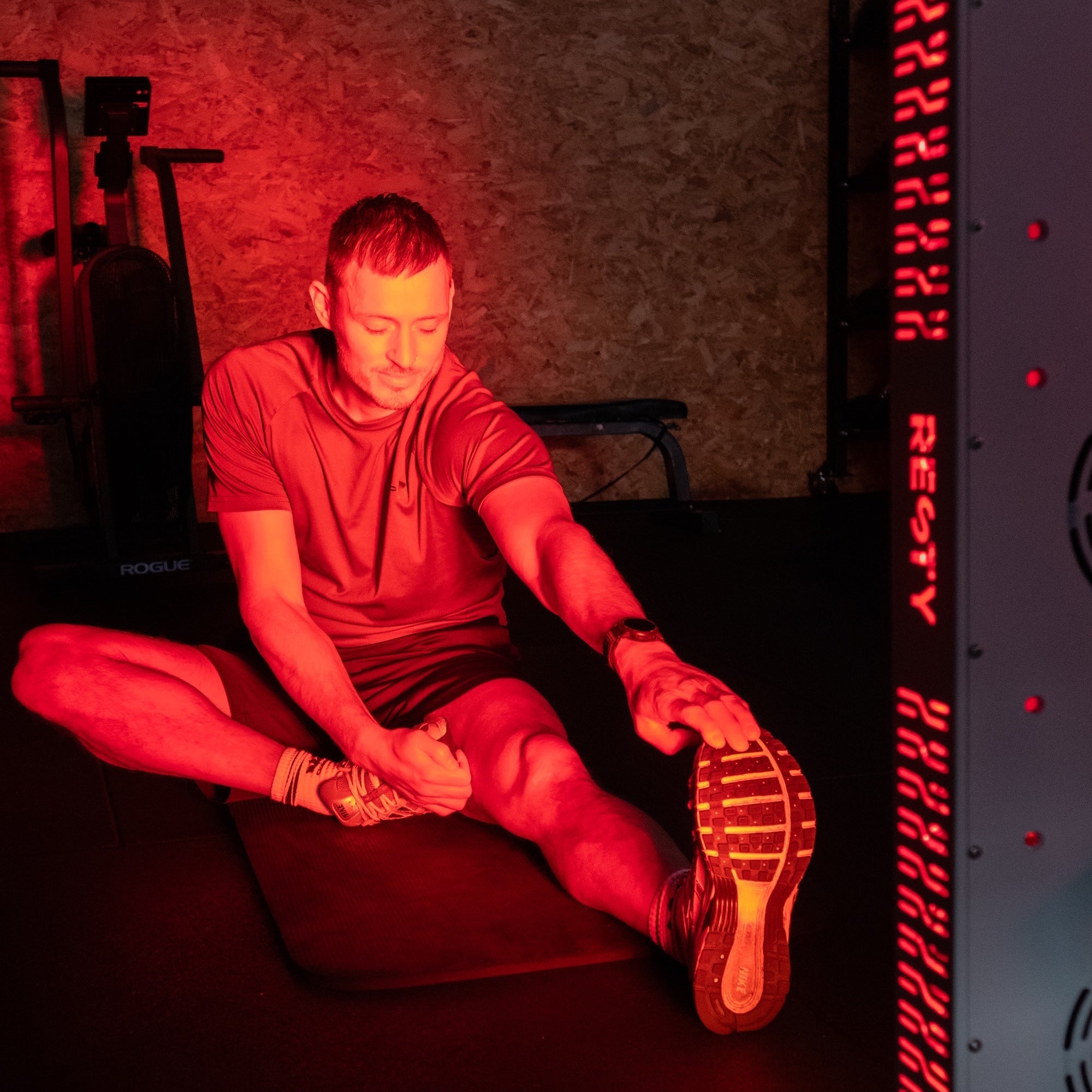 Man stretching beside an illuminated Resty MARS 1000 red light panel in a gym
